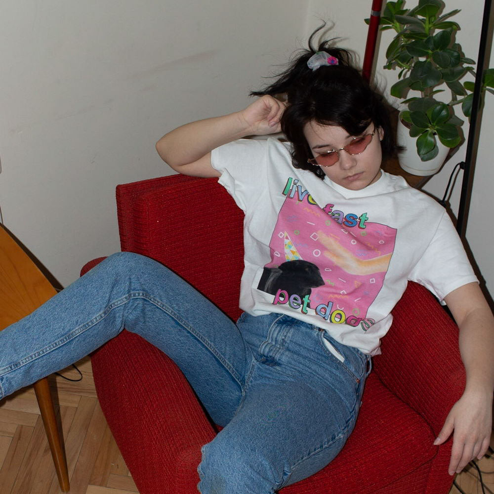 Person sitting on a red chair wearing a colorful graphic t-shirt and blue jeans.